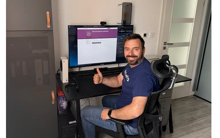 Jozef Petluš sedí za pracovným stolom s počítačom a zdvihnutým palcom naznačuje, že úspešne absolvoval certifikáciu na Odoo 19.